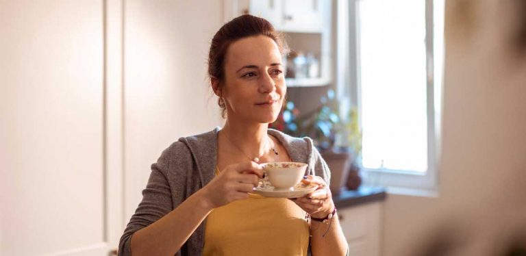 A person standing in a kitchen and sipping tea.