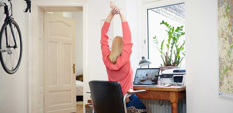 A woman sitting at her desk at home, raising her arms above her head to stretch.