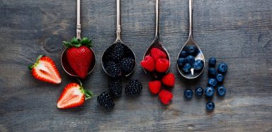 Four spoons with four different types of sorted fruit on them: strawberries, blackberries, raspberries and blueberries.