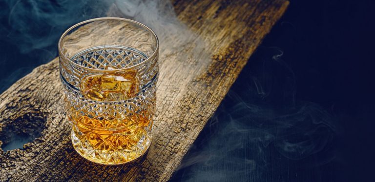 A glass of whiskey on a wooden table.