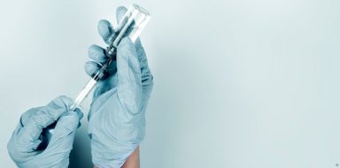 A pair of hands wearing medical gloves, filling a needles with injectable medicine.